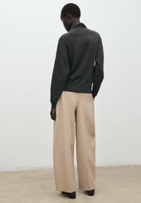 Temno sivi pulover z visokim ovratnikom, sproščenim krojem in širokimi bež hlačami. Obleka ima gladko teksturo in nevtralen barvni izbor.