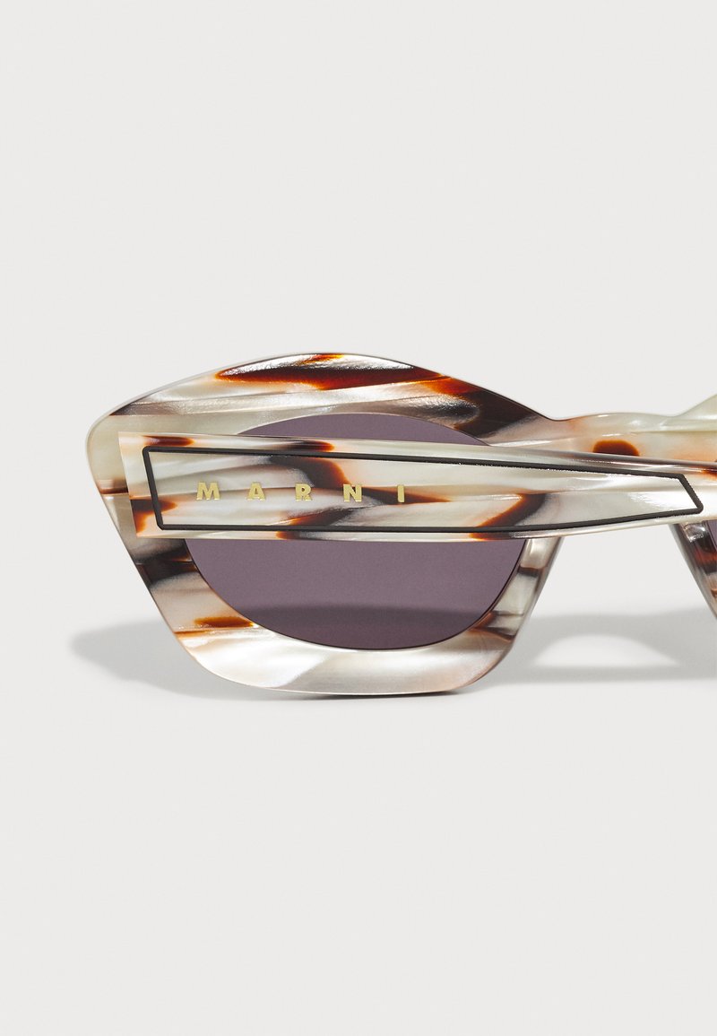 Lunettes de soleil angulaires avec une monture en acétate écaille de tortue, dotées d'un verre violet audacieux et d'un logo doré sur une barre d'accent argentée.