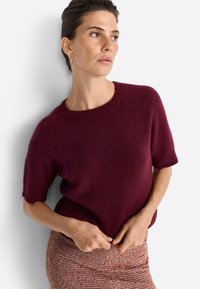 Burgundy short-sleeve knit sweater with a round neckline, soft texture, and relaxed fit, paired with a brown checkered skirt.