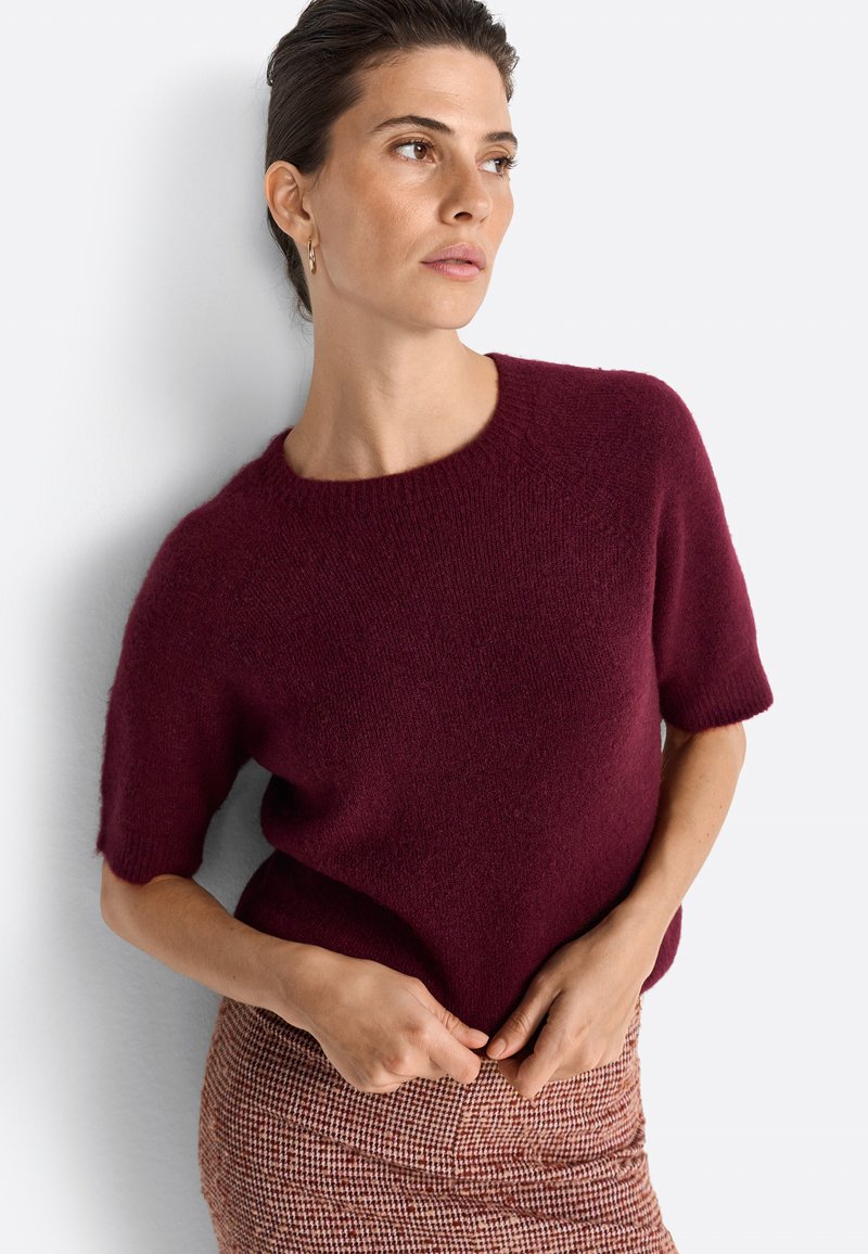 Burgundy short-sleeve knit sweater with a round neckline, soft texture, and relaxed fit, paired with a brown checkered skirt.