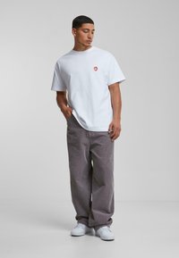 Witte katoenen t-shirt met een klein rood logo op de borst. Gecombineerd met losvallende, verticaal gestreepte grijze corduroy broek en witte sneakers.