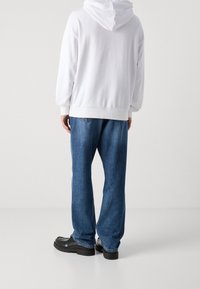 Sudadera blanca de algodón con capucha, combinada con vaqueros de mezclilla azul holgados y zapatos negros. Textura suave, ajuste casual y sin patrones visibles.