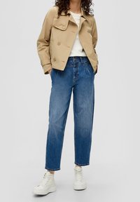 Beige cropped jacket with double-breasted design, blue denim relaxed-fit jeans, and white chunky sneakers. Smooth fabric and casual style.