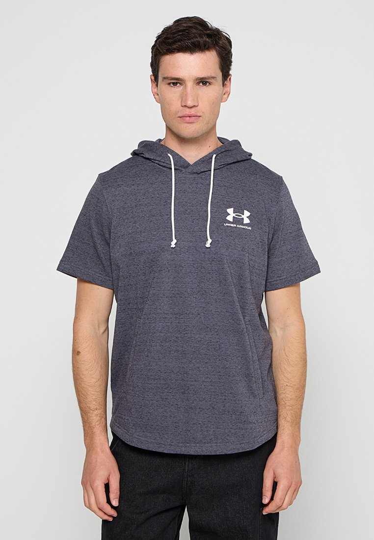 Un jeune homme aux cheveux bruns courts portant un hoodie à manches courtes gris foncé avec le logo Under Armour sur la poitrine, se tenant devant un fond uni.