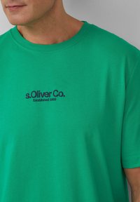 Zielona bawełniana koszulka z okrągłym dekoltem. Posiada nadrukowane logo w ciemnoniebieskim kolorze: "s.Oliver Co. Założona w 1969 roku." Krótkie rękawy.
