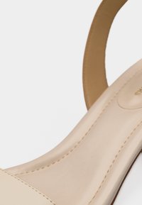 Κοντινό πλάνο ενός μπεζ σανδαλιού με λουριά από λείο δέρμα και ορατές ραφές στην εσωτερική σόλα και το λουρί της φτέρνας.