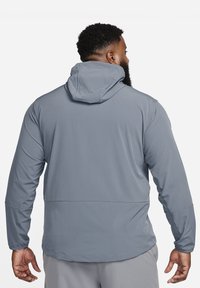 Kerge hall kapuutsiga jakk sileda tekstuuri, pikkade varrukate ja lihtsa disainiga. Omab tagumise õmbluse ja reguleeritava kapuutsiga.