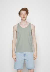 Un débardeur en coton vert clair à col rond, porté avec un short en denim bleu clair. Le tissu semble doux et respirant.