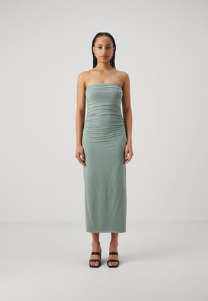 Abito midi aderente senza spalline in tessuto verde tenue con una texture liscia e dettagli arricciati. Indossato con tacchi neri con cinturino.