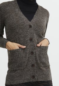 Brun stickad cardigan med V-ringning, fem mörka knappar, ribbade fickor och texturerat tyg, med en avslappnad passform och långa ärmar.