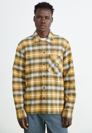 Camicia in flanella a quadri gialli e verdi con colletto button-down, taschino sul petto e maniche lunghe. Tessuto morbido, con bottoni neri.