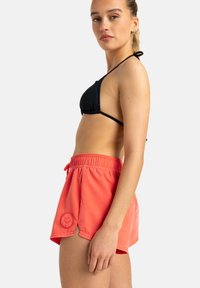 Schwarzer Bikini-Oberteil und korallenfarbene Badeshorts mit elastischem Taillenbund und Kordelzug. Die Shorts verfügen über seitliche Schlitze und ein Logodetail am Saum.