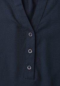 Gros plan sur l'avant d'une chemise bleu foncé montrant trois boutons ronds et un col en V.