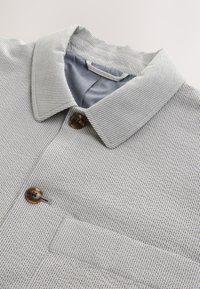 Gray and white striped shirt with a classic collar, brown buttons, and a chest pocket. Textured fabric with a smooth inner lining.