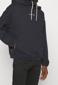 Marinblå huvtröja i mjukt material med en frontficka av typ kangaroo och vita snörningar, med en logotyp på bröstet.