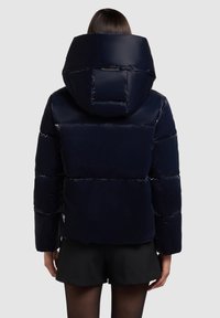 Námornícky puffy kabát má lesklý povrch, oversized kapucňu, skrátený dizajn a prešívanú textúru s elastickými manžetami a zipsovými vreckami.