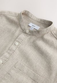 Chemise beige clair texturée avec col mao, boutons sur le devant, poche poitrine et étiquette de marque "NEXT" en taille moyenne.