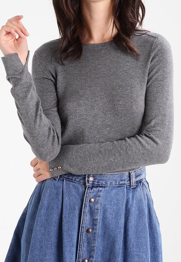 Pull gris à manches longues en tissu tricoté, doté d'un col rond et de détails subtils de couture, associé à une jupe bleue à boutons sur le devant.