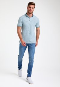 Gai zils polo krekls ar teksturētu rakstu, īsām piedurknēm un apkakli. Saskaņots ar pieguļošām zilām džinsām un baltām sporta kedām.