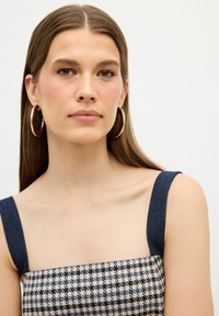 Top s denim a vzorem houndstooth s tmavě modrými pásky. Obsahuje velké kruhové náušnice. Neutrální pozadí zvýrazňuje design.