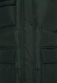 Mørkegrønne polstret jakke med en glat overflade, der har to frontlommer og knaplukning. Der er ingen synlige mønstre eller udsmykninger.