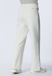 Pantaloni della tuta bianchi con vita elastica, gambe dritte, tasche laterali e texture liscia. Abbinati a sneakers di colore chiaro.