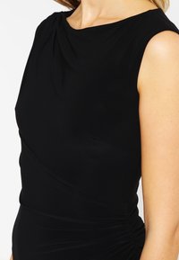 Czarna bezrękawnikowa sukienka z drapowanym dekoltem, dopasowanym gorsetem i marszczeniem z boku, wykonana z gładkiego, elastycznego materiału.