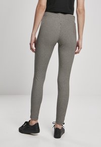 Leggings ajustados en un patrón de cuadros en blanco y negro, con una cinturilla alta y una textura suave. Llevados con zapatillas negras de cordones.