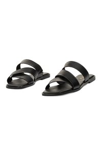 Sandalias de slide de cuero negro con tres correas anchas y una suela plana. Textura lisa y diseño minimalista. Adecuadas para vestir de forma casual.