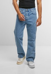 Hellblaue Jeans im geraden Schnitt mit seitlichen Druckknöpfen und fünf Taschen. Getragen mit weißen und beigen Sneakers.