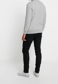Felpa grigia con maniche lunghe, polsini a coste e scollatura rotonda, abbinata a jeans neri slim-fit e scarpe bianche alte.