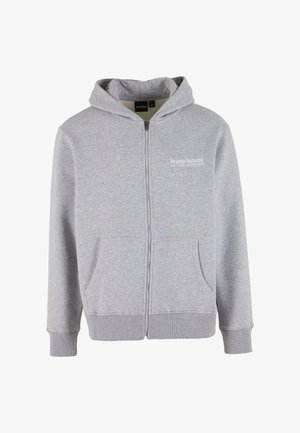 Šedá mikina na zip vyrobená z měkké látky, s velkými předními kapsami, žebrovanými manžetami a kapucí se stahovací šňůrkou. Na hrudi je malá značka.