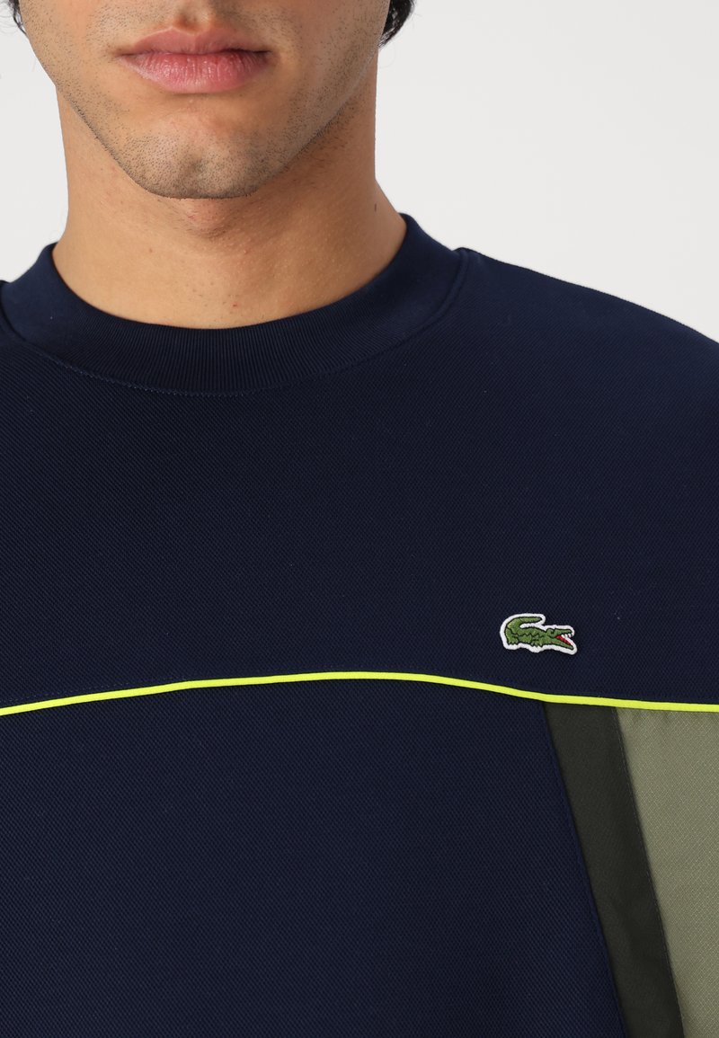 Sweat-shirt bleu marine avec un tissu texturé, doté d'une touche de vert et d'un petit logo de crocodile brodé sur la poitrine.