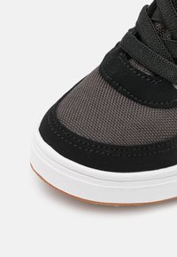 Czarne i szare sneakersy z teksturowanym materiałowym wierzchem, płaskimi czarnymi sznurowadłami, białą podeszwą środkową i brązową gumową podeszwą.