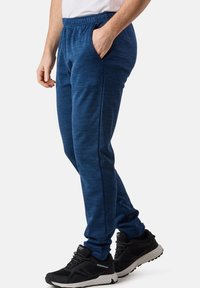 Marineblaue Jogginghosen aus strukturiertem Stoff mit elastischem Bund, seitlichen Taschen und schmal zulaufendem Bein, kombiniert mit schwarzen Sportschuhen.