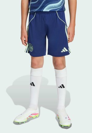 Shorts de sport bleu marine avec des accents verts et un logo, associés à des chaussettes blanches montantes à rayures noires et des crampons de football colorés.
