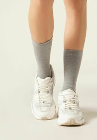 Hvide sportsko med grå accenter, parret med knæhøje grå sokker. Sneakers har et mesh-design og en struktureret sål.