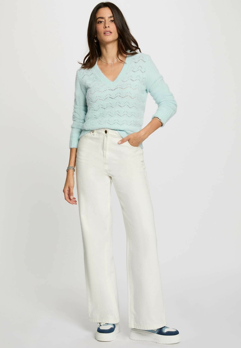 Maglione azzurro chiaro a collo a V con motivo a zigzag, abbinato a jeans bianchi a vita alta e gamba larga e sneaker con dettagli blu.