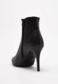 Bottine en cuir noir avec un talon aiguille haut et une fermeture éclair latérale. Elle présente une texture lisse et une silhouette courbée.