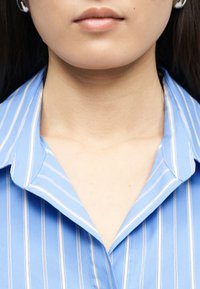 Κοντινό πλάνο του κάτω μέρους του προσώπου και του λαιμού ενός ατόμου που φοράει πουκάμισο με ρίγες μπλε και λευκές και κολάρο.