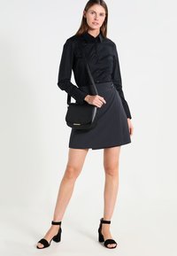 Zwarte button-up blouse, grijzende wikkelrok, zwarte schoudertas met gouden accenten, chunky zwarte haksandalen. Zachte texturen en een op maat gemaakte pasvorm.
