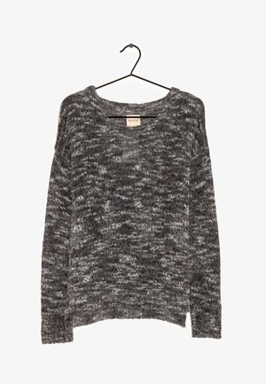 Pull en maille grise avec une coupe décontractée, présentant un tissu doux et texturé ainsi qu'un col rond, suspendu à un cintre en métal noir.