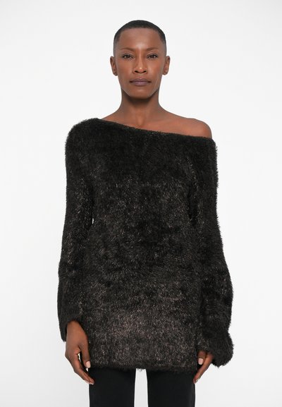 Zwarte fuzzy trui met een off-shoulder ontwerp, lange mouwen en een textuurfinish. Gecombineerd met zwarte, strak zittende broeken.