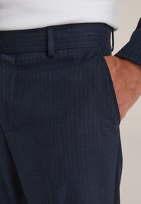 Mörkblå randiga byxor i en strukturerad tygkvalitet, med smal passform och sidofickor. Midjan är rak och slät.