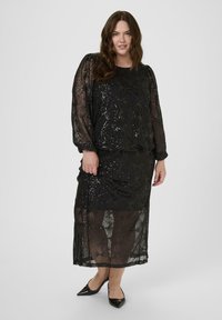 Black dress featuring a sheer overlay with geometric patterns and sequins, long sleeves, and a fitted silhouette. Black heels complete the look.