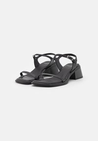 Sandales noires à lanières, ouvertes à l'avant, avec une boucle à la cheville et des talons blocs bas, sur un fond blanc uni.