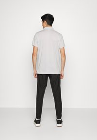 Lys grå polo skjorte med nedfellbar krage, korte ermer og avslappet passform, kombinert med svarte bukser og svarte sneakers.