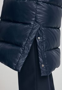 Mörkblå puffjacka med quiltad textur, med tryckknappar och en liten sprund i nederkant för bättre rörelse och design.