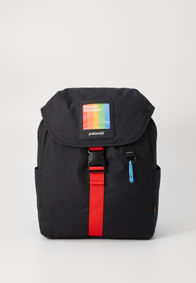 Mochila preta em ripstop com uma forma estruturada, alça vermelha, aba superior e um patch frontal exibindo um logótipo multicolorido. Acento em zíper azul.