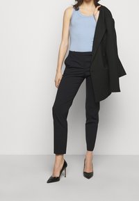 Top blu ribbed abbinato a pantaloni neri su misura e scarpe nere con tacco alto, con un blazer nero appoggiato su una spalla.